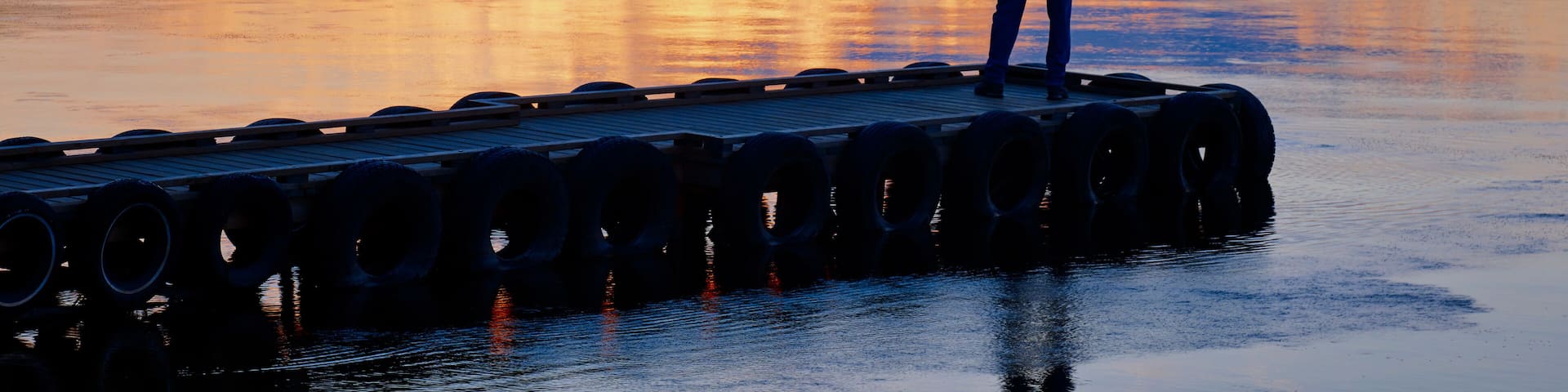 Silhouette Of A Person Standing At The End Of A Dock Looking Out Over A Tranquil Lake At Sunset, Gregoire Lake Provincial Park; Alberta, Canada