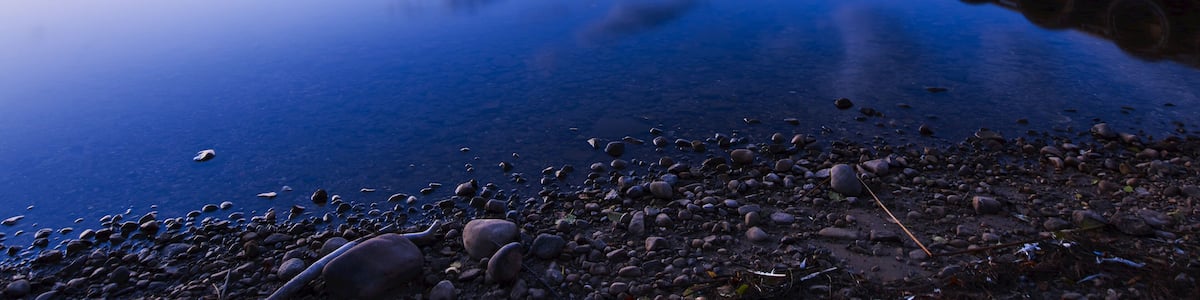 Glowing horizon at sunset reflected in tranquil water of Gregoire Lake with a dock leading out from the shore in the foreground; Fort McMurray, Alberta, Canada