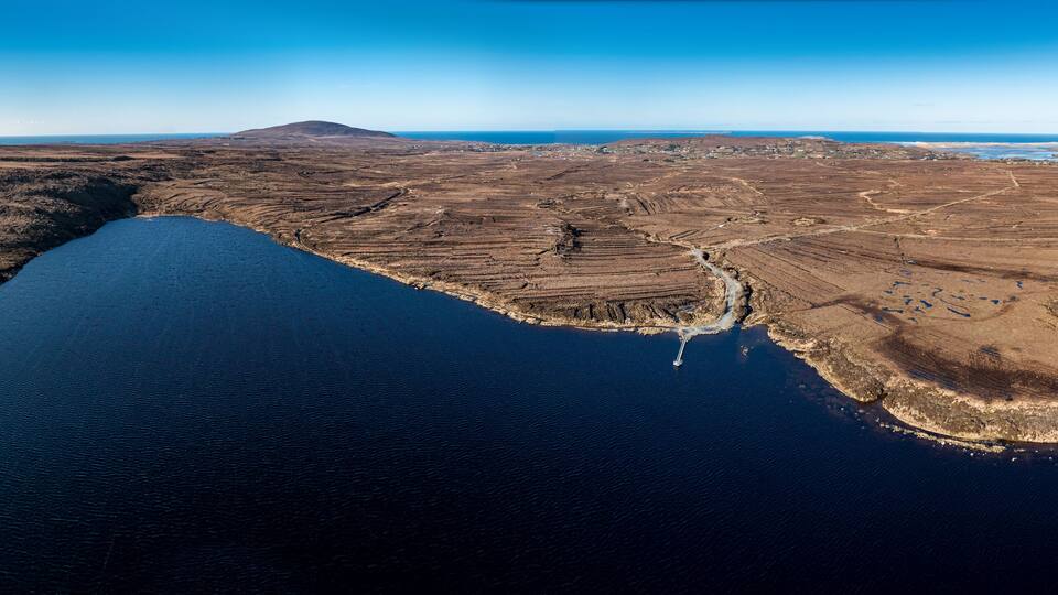 An aerial view of a coastal landscape with a large body of water, terraced fields, and a distant mountain.