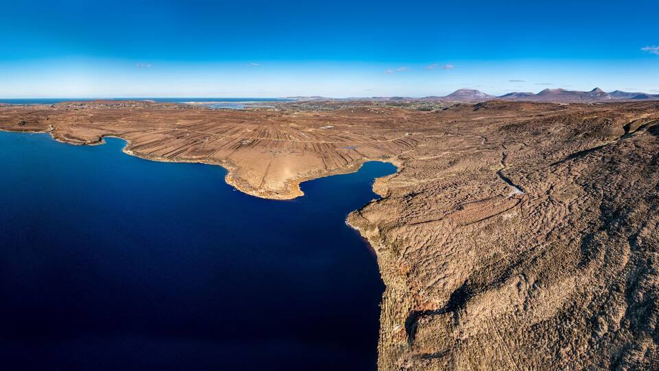 A vast lake surrounded by rugged terrain and distant mountains.