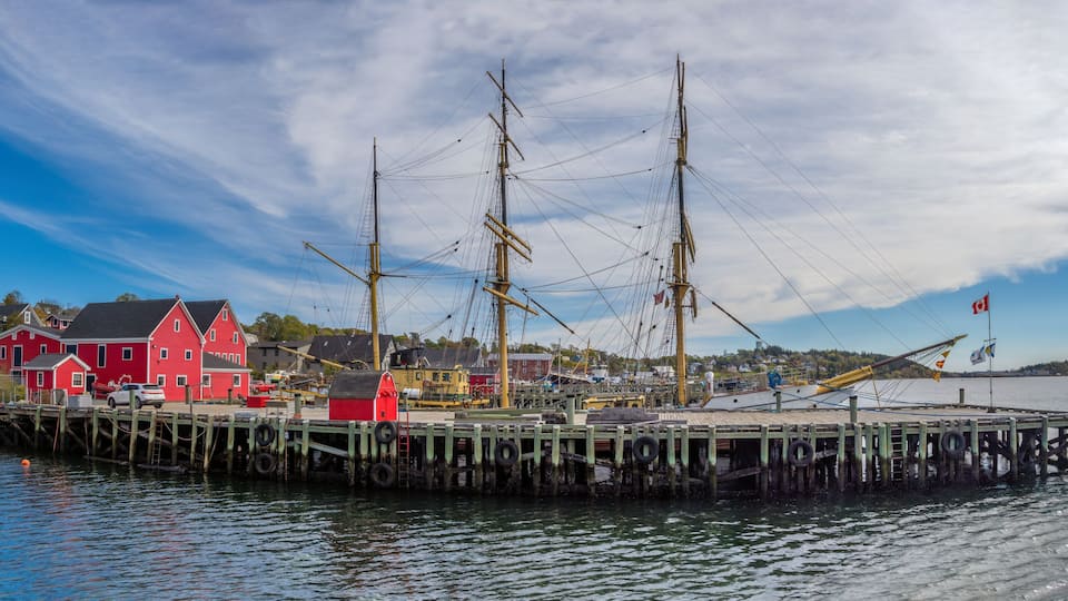 A historic ship docked at a pier with colorful buildings in the background.