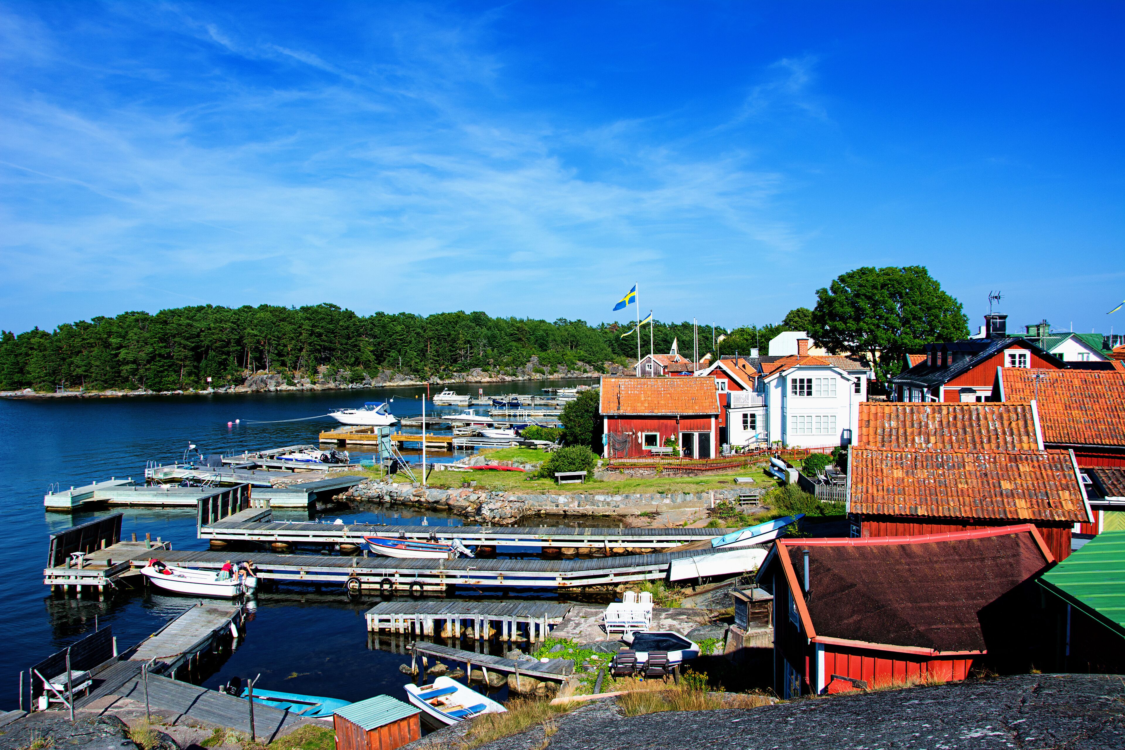 A harbor with boats docked, a red-roofed building, and a Swedish flag.