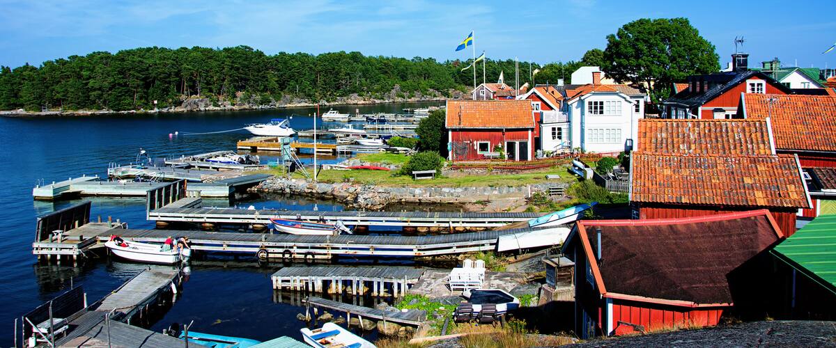 A harbor with boats docked, a red-roofed building, and a Swedish flag.