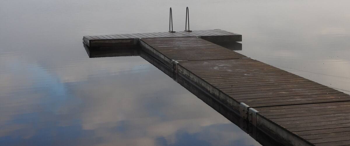 A wooden pier extending into calm water with a misty background.