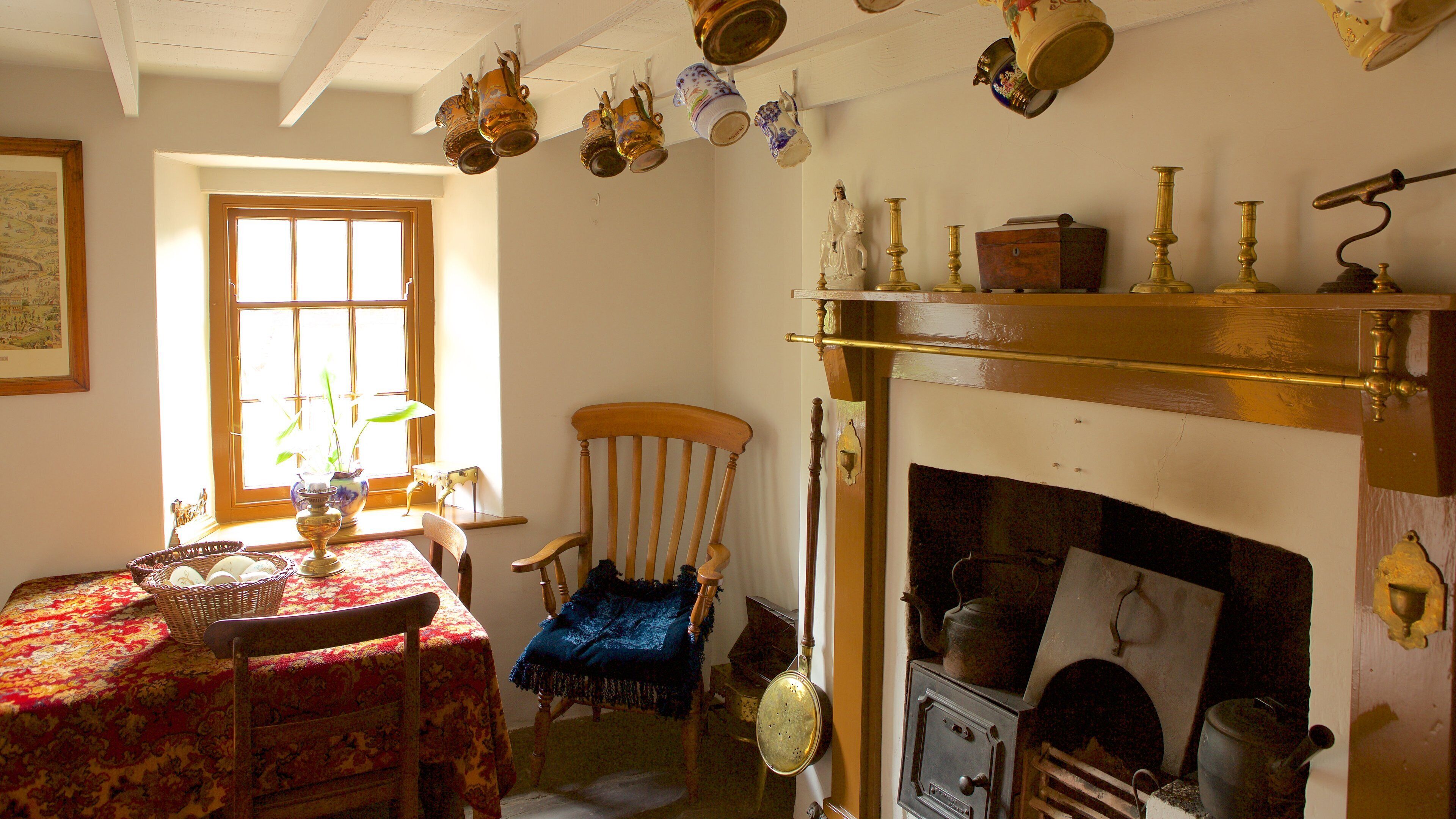 Una habitación tradicional con chimenea, una mesa con mantel floral y varios objetos antiguos colgados en la pared.