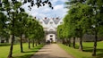 A pathway lined with trees leading to a white building with a stone archway.