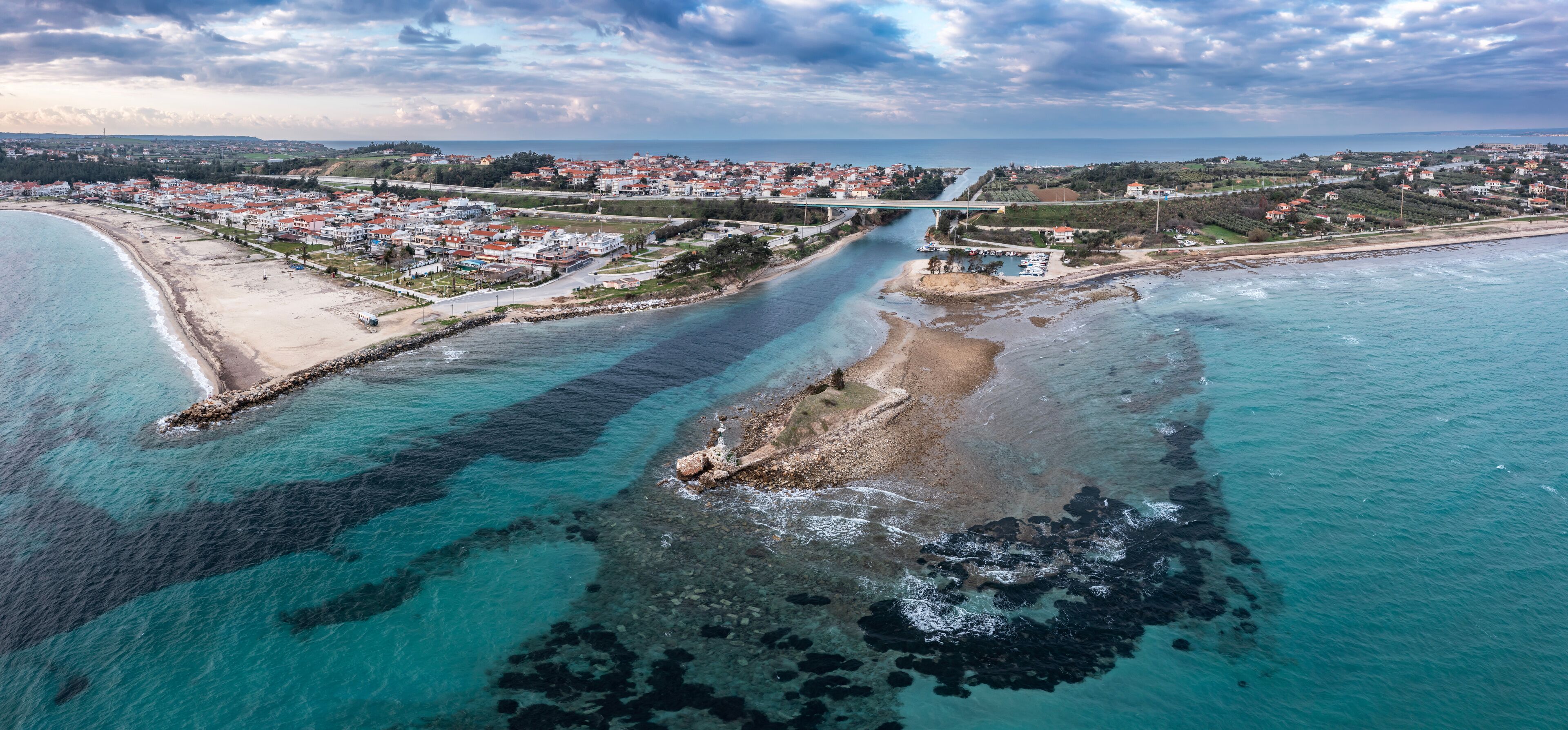 An aerial view of a coastal town with a bridge, clear turquoise waters, and a sandy beach.