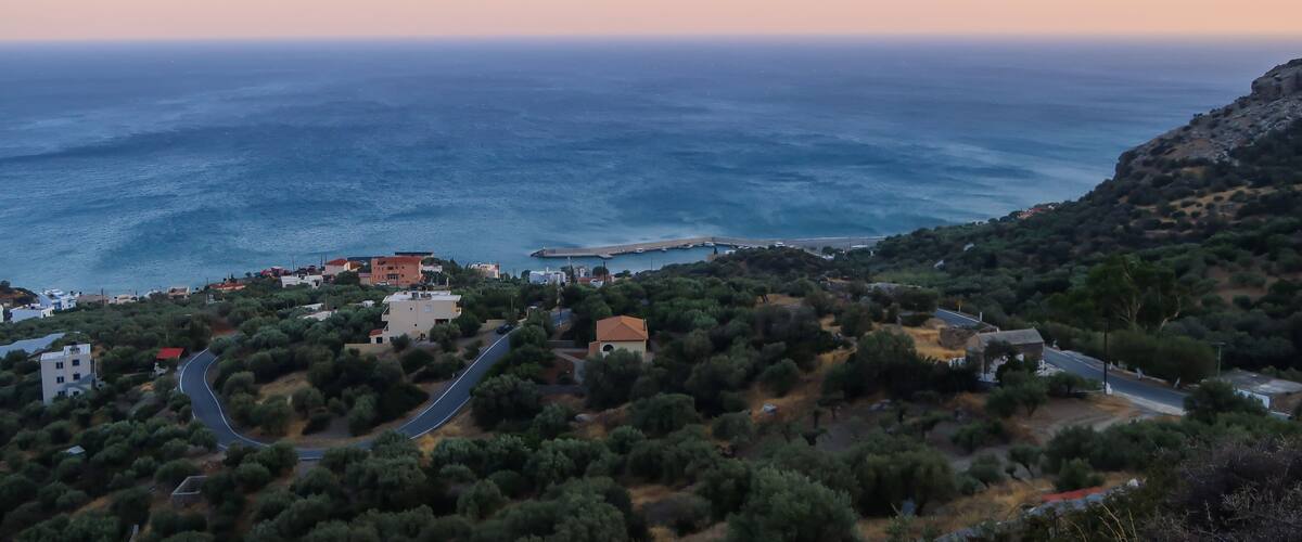 A coastal landscape with a winding road, buildings, and a rocky hillside.