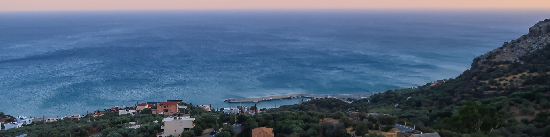 A coastal landscape with a winding road, buildings, and a rocky hillside.