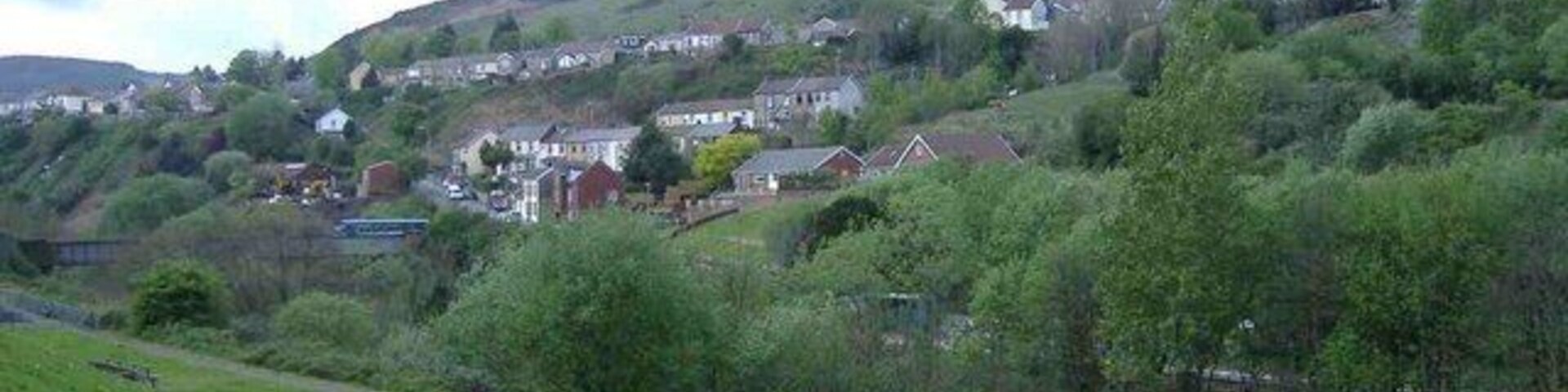 Una ladera verde con casas y una colina al fondo.