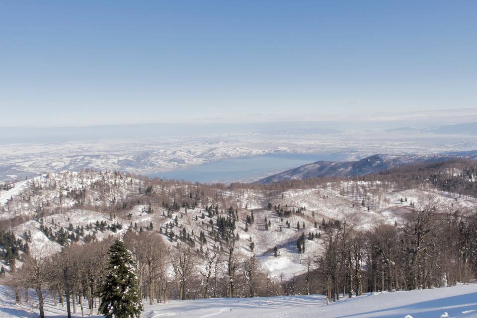 Paisagem montanhosa coberta de neve, com um lago e céu azul límpido.