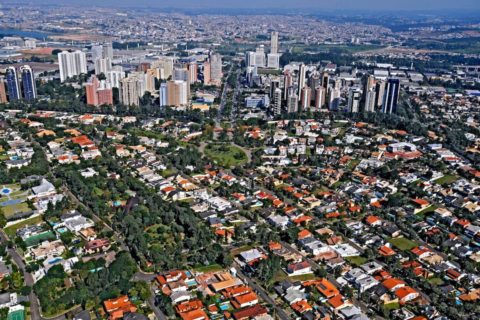 Vista aérea de uma cidade com áreas residenciais densas, vários edifícios altos e uma combinação de áreas verdes.