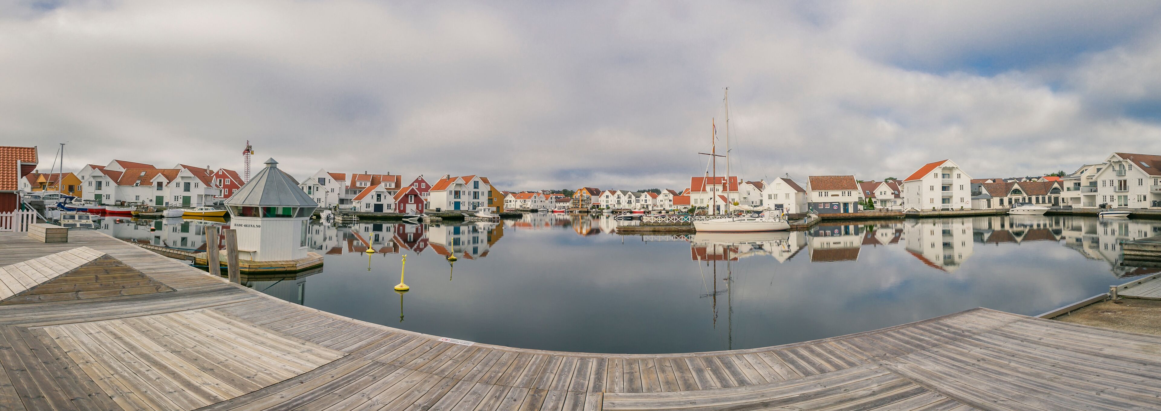 A calm harbor with wooden docks and a row of colorful houses reflecting in the water.