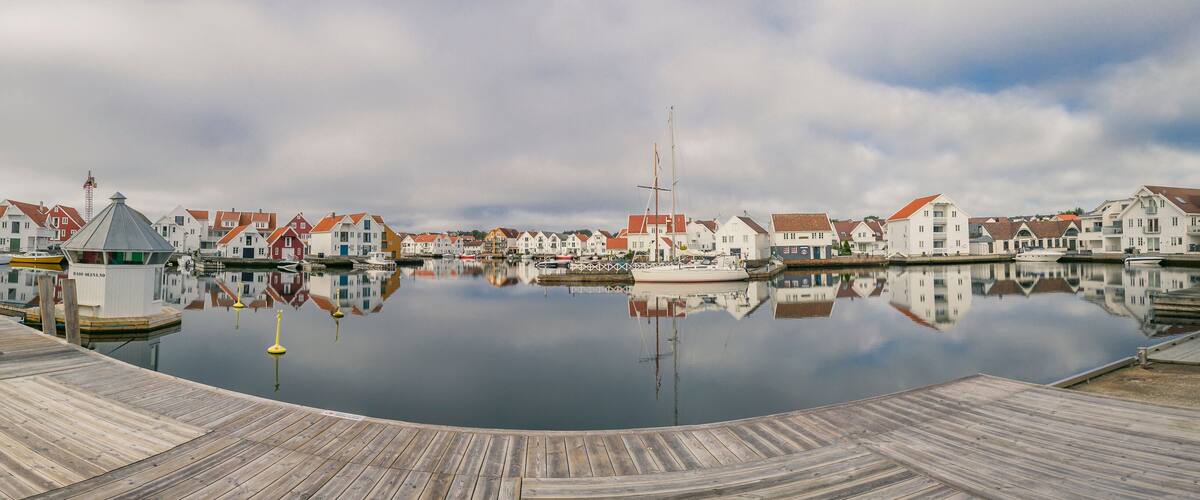 A calm harbor with wooden docks and a row of colorful houses reflecting in the water.