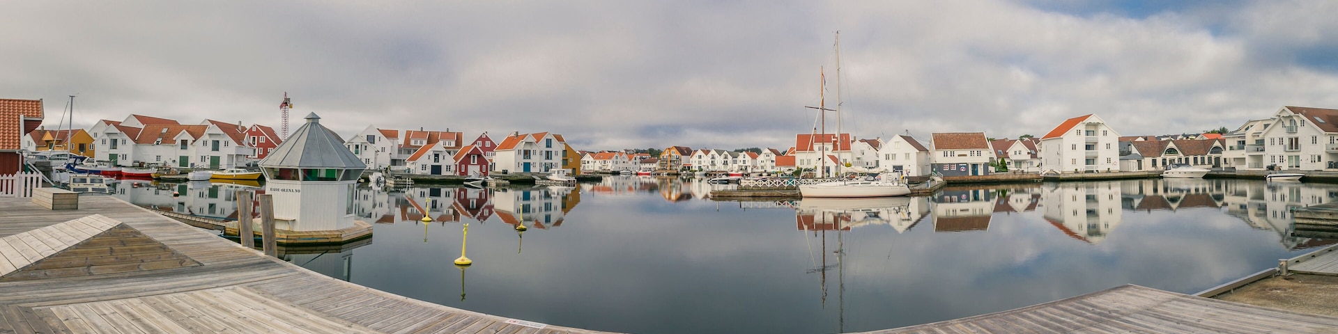 A calm harbor with wooden docks and a row of colorful houses reflecting in the water.