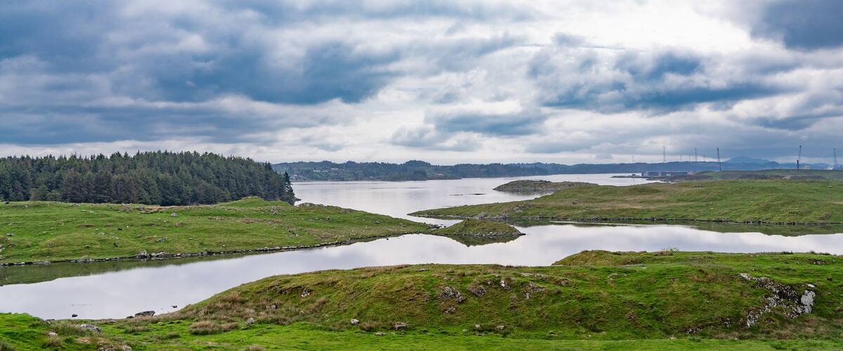 A landscape with a lake surrounded by green hills and a forested area in the distance.