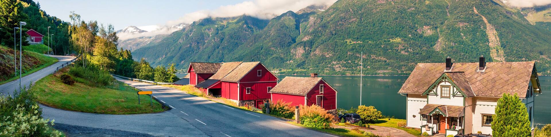 A scenic road with red houses and a lake surrounded by mountains.