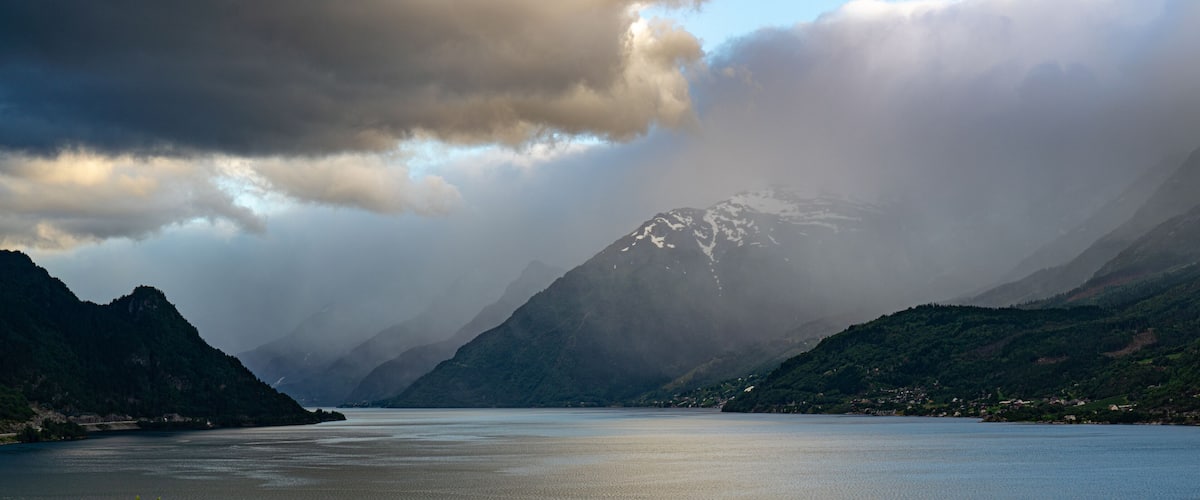 A lake surrounded by mountains with snow-capped peaks and dense forests.