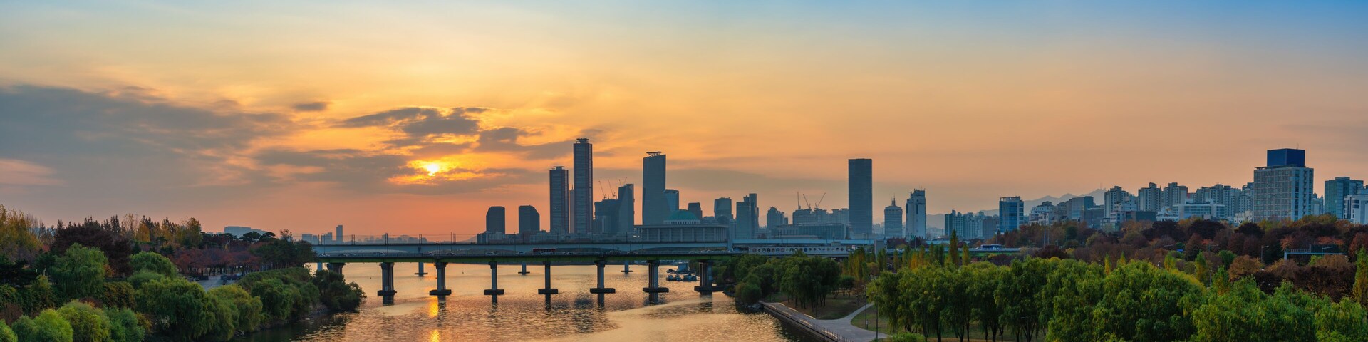 Un horizonte urbano al atardecer, con un río y un puente en primer plano.