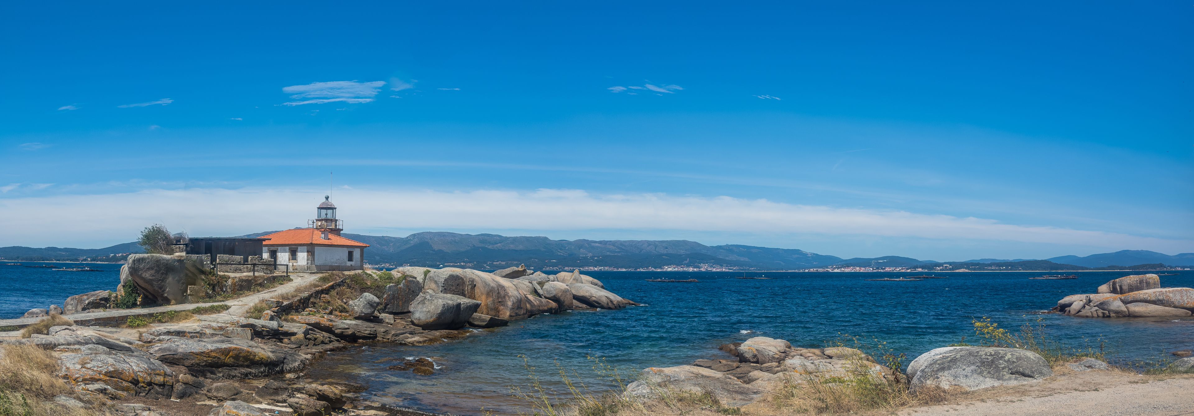 Panoramic view of Punta Cabalo Lighthouse on Arousa Island, Galicia, Spain, set among granite rocks overlooking the blue waters of the Atlantic Ocean.