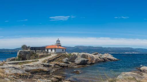 Panoramic view of Punta Cabalo Lighthouse on Arousa Island, Galicia, Spain, set among granite rocks overlooking the blue waters of the Atlantic Ocean.