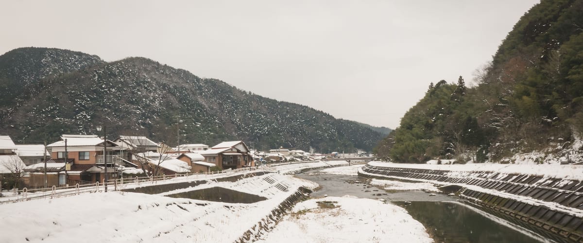 A snow-covered landscape with a river, buildings, and mountains.