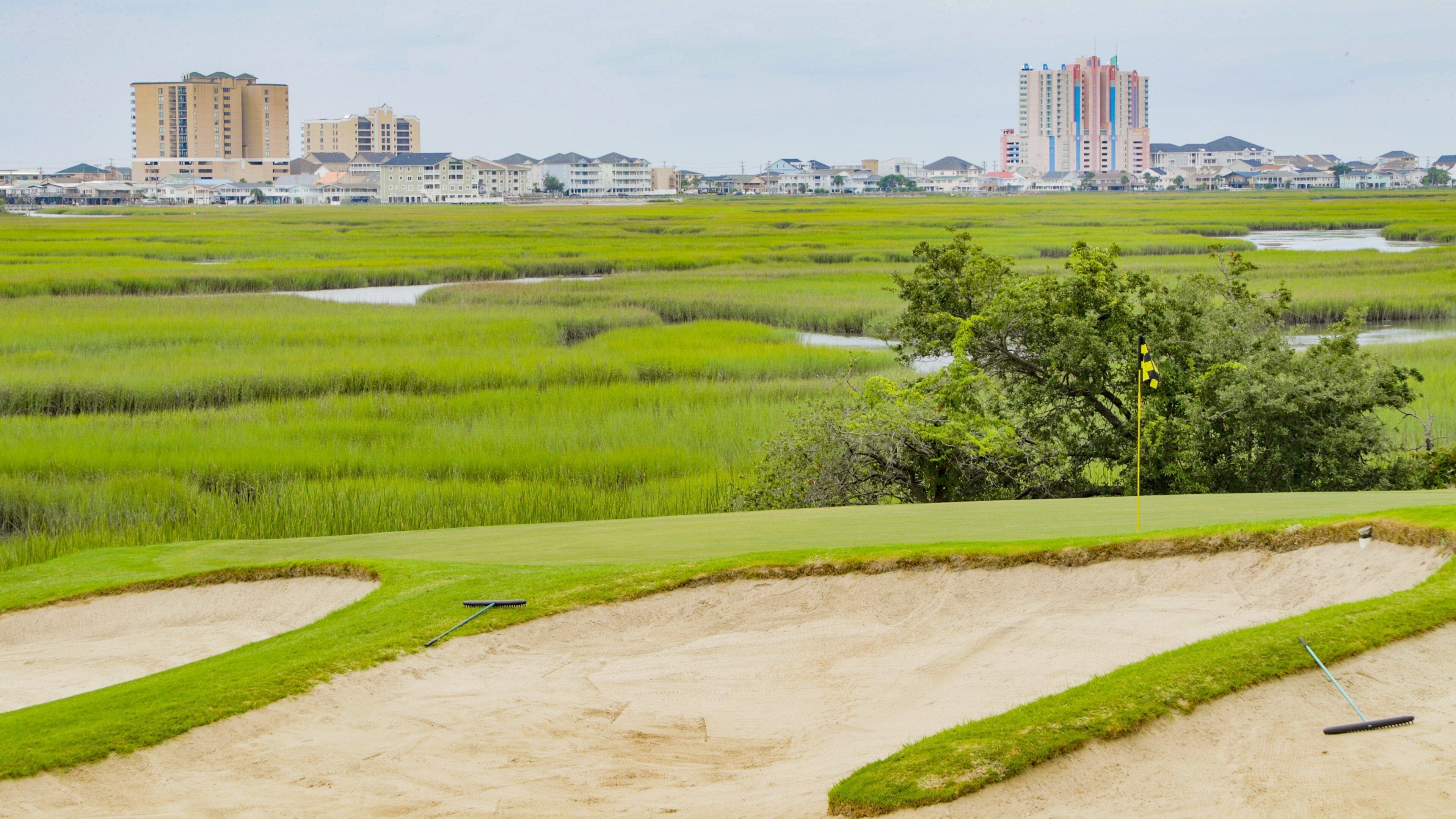 Um campo de golfe com bunkers de areia e paisagem urbana ao fundo.