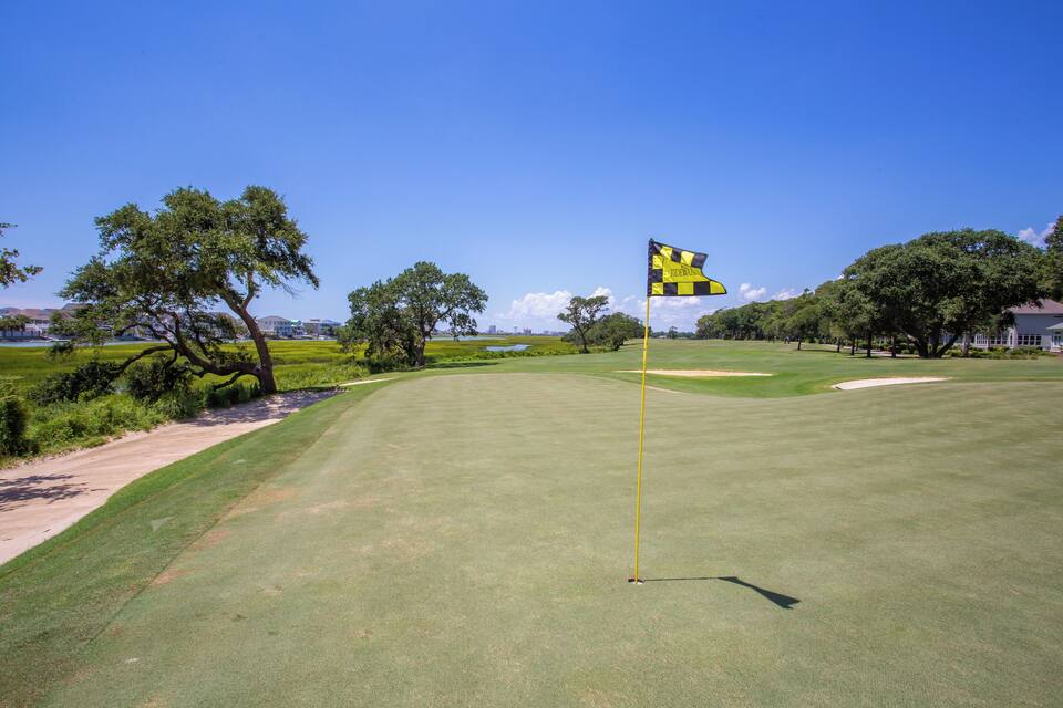 A golf course with a flag, trees, and a clear sky.
