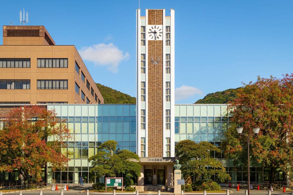 Un edificio moderno con una torre de reloj, rodeado de árboles y un cielo despejado.