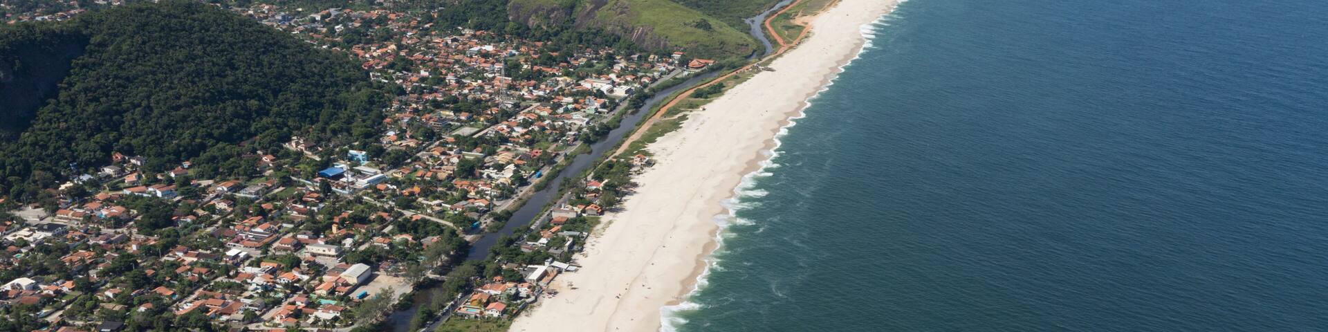 An aerial view of a coastal city with a long beach, dense urban area, and surrounding hills.