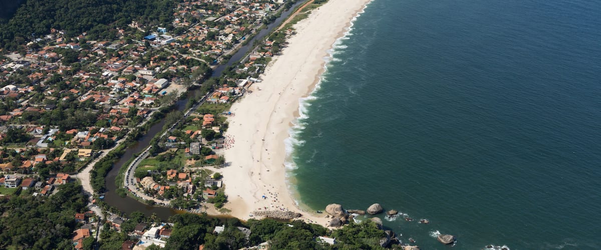 An aerial view of a coastal city with a long beach, dense urban area, and surrounding hills.