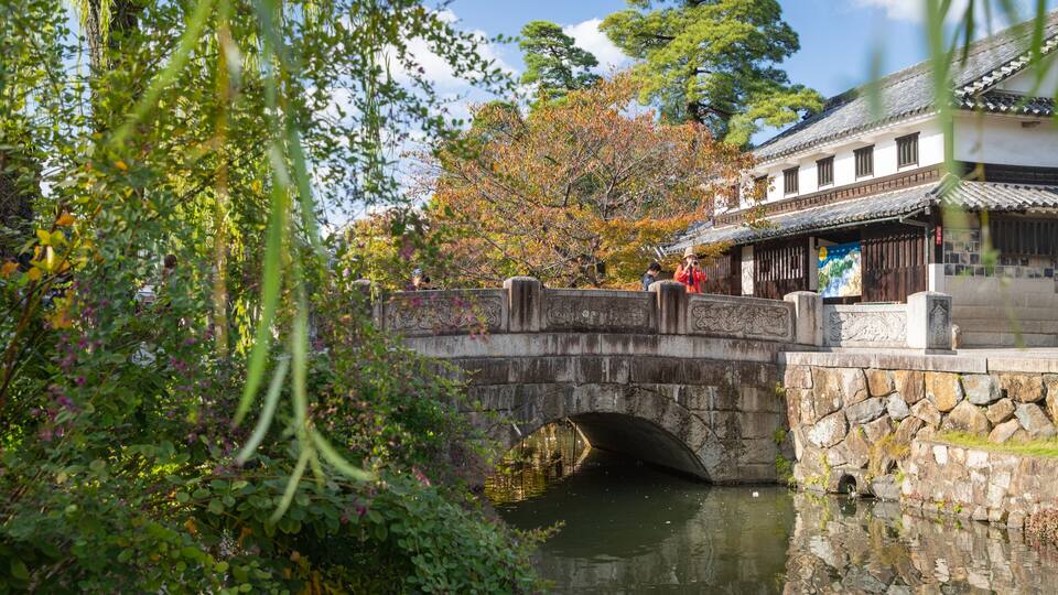 A stone bridge over a calm river, surrounded by lush greenery and autumn trees.