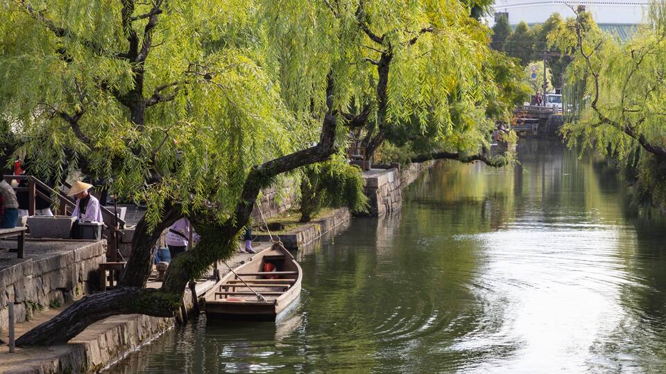 A calm river with boats, a stone bridge, and people in traditional attire.