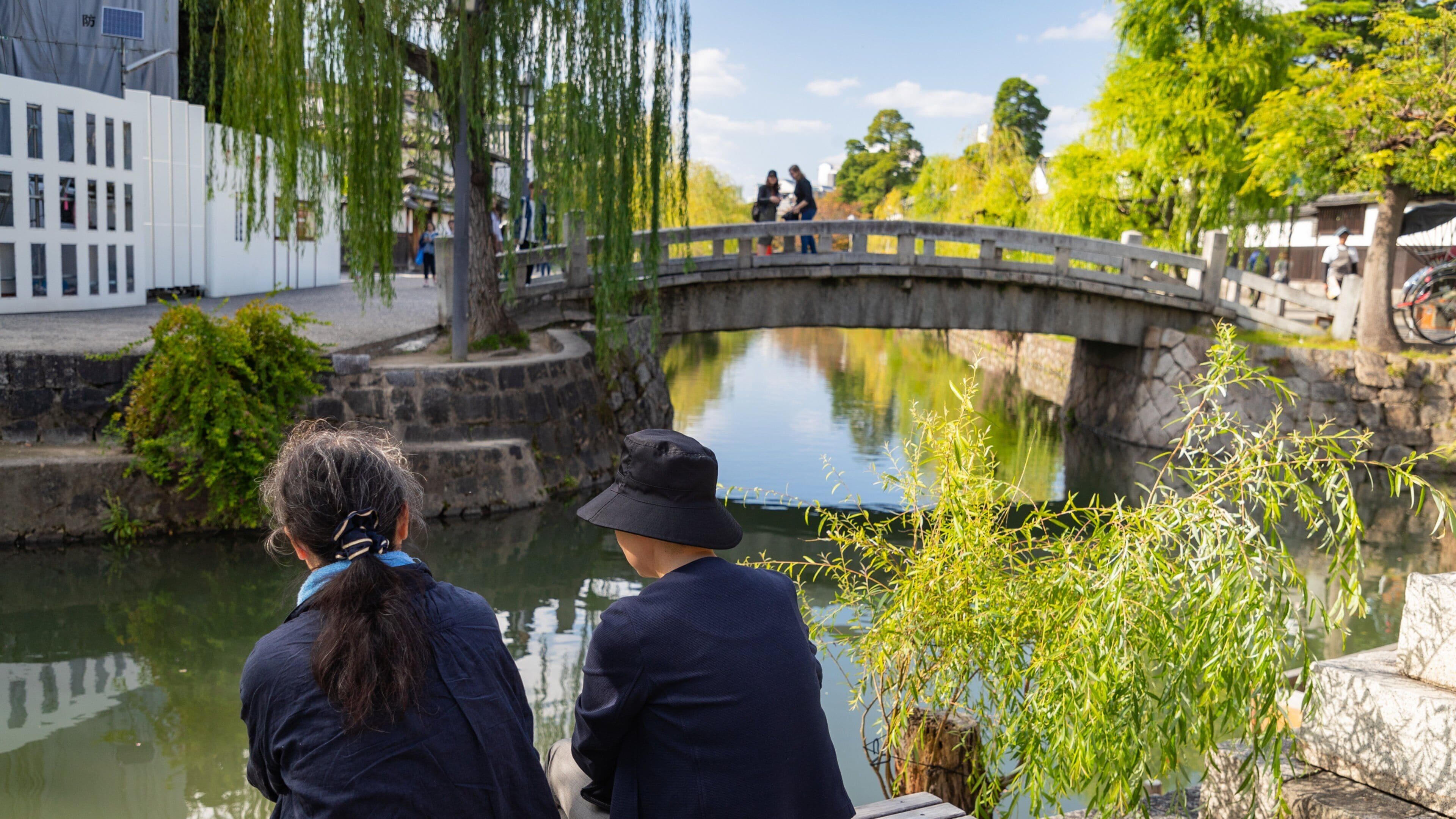 Un puente de piedra sobre un río tranquilo, rodeado de vegetación y edificios.
