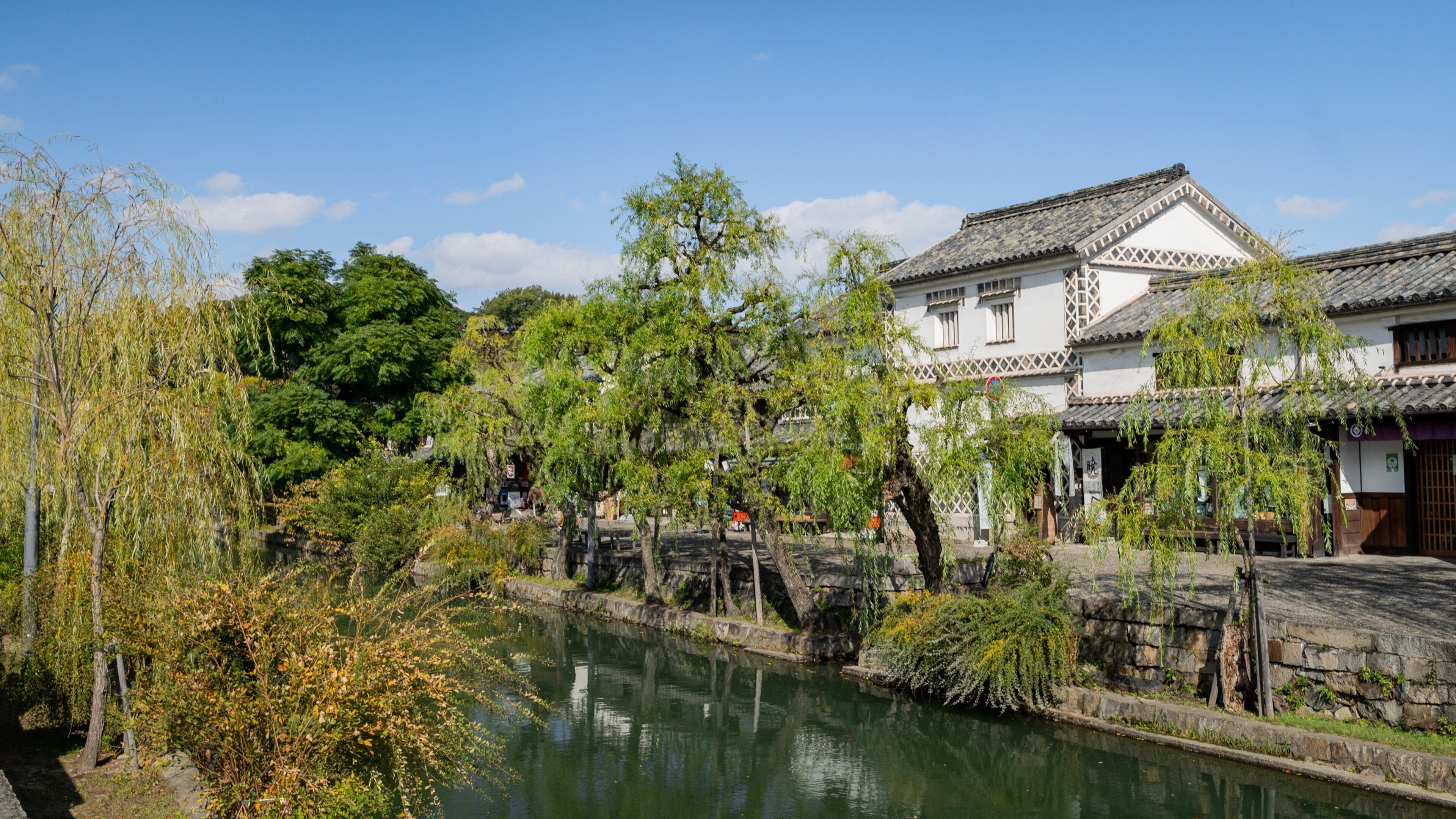 A traditional Japanese building with a tiled roof, a stone bridge, and a calm river.
