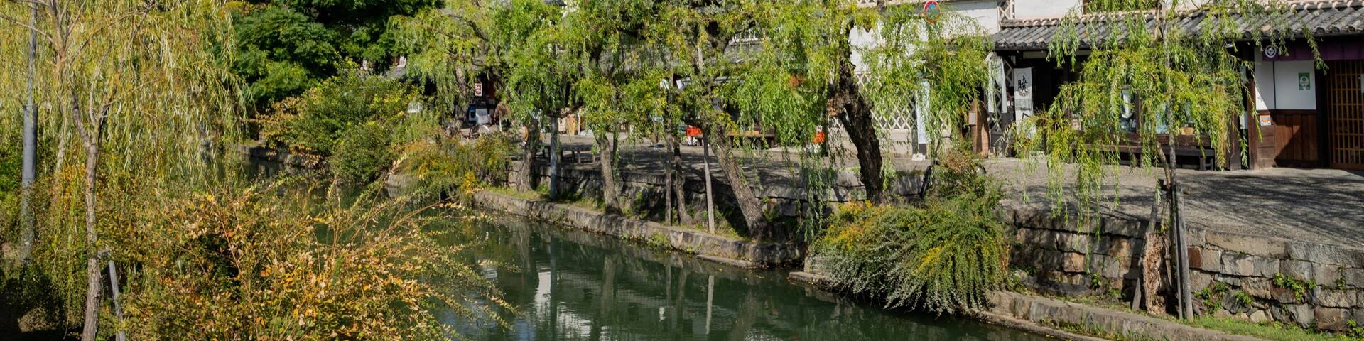 A traditional Japanese building with a tiled roof, a stone bridge, and a calm river.