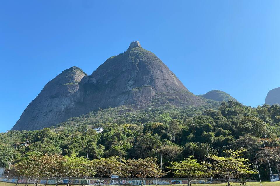 A mountain with a prominent peak, surrounded by lush greenery and a clear blue sky.