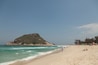 A beach with clear turquoise waters, a sandy shore, and a prominent hill in the background.