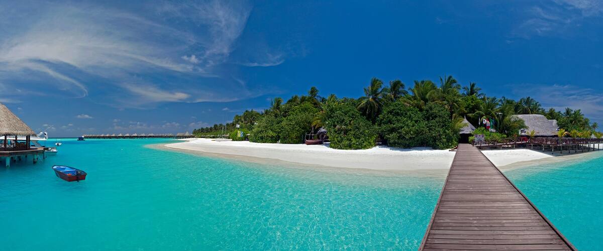 A wooden pier leading to a white sandy beach, surrounded by turquoise waters and lush greenery.