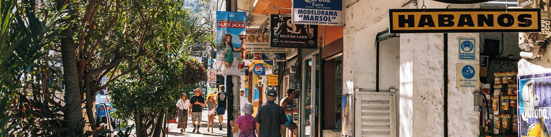 Uma rua estreita repleta de lojas e placas, incluindo uma placa grande da 'Habanos'.