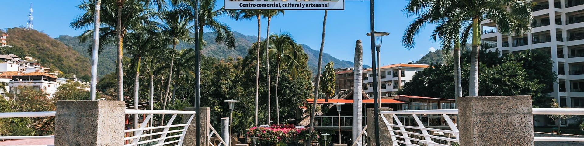 A bridge with a sign reading 'Isla Riquelme Centro comercial, cultural y artesanal' leading to a commercial area with palm trees and buildings.
