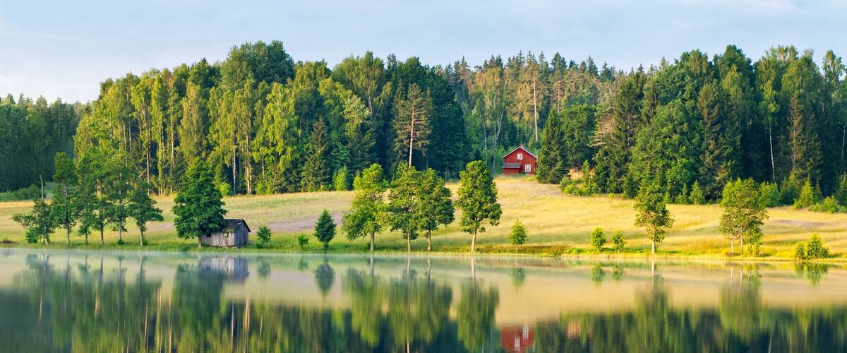 A serene lake with reflections of trees and a red cabin.