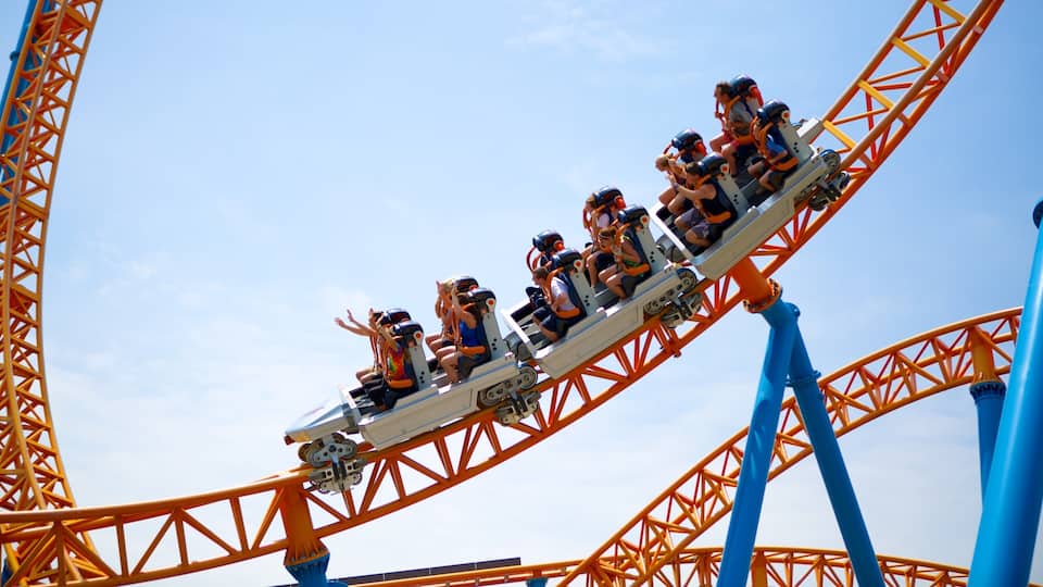 A roller coaster with riders in orange and blue seats, a clear blue sky, and a steel structure.