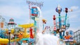 Ein Wasserpark mit einer Fontäne, einem Riesenrad und verschiedenen bunten Spielgeräten.