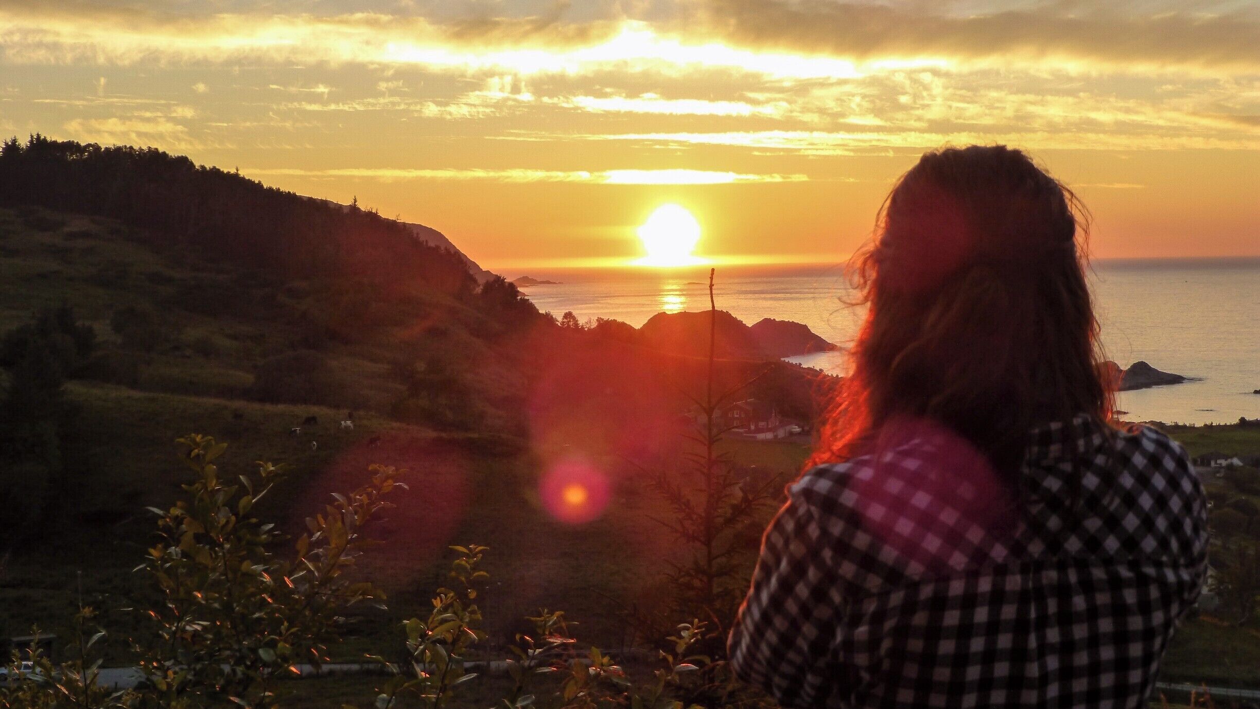 A sunset over a coastal landscape with hills and a body of water.