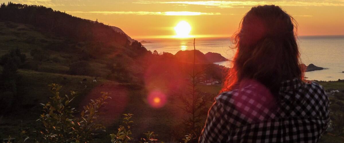 A sunset over a coastal landscape with hills and a body of water.