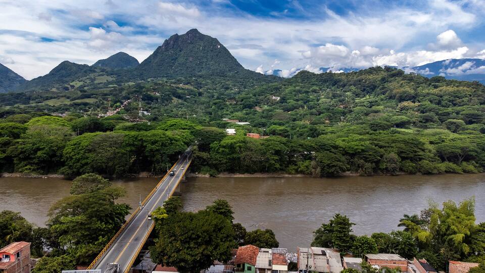 A river with a bridge, lush green hills, and a mountain in the background.