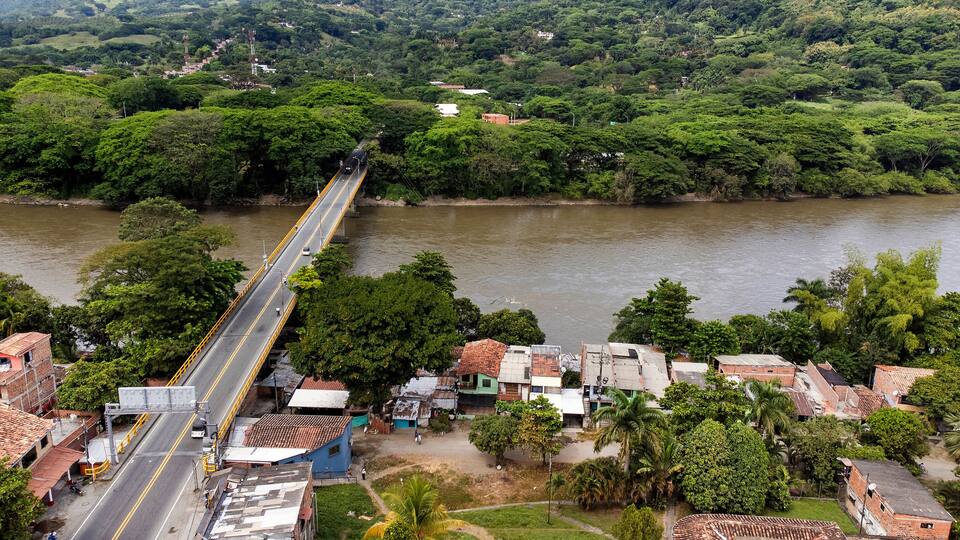 A river with a bridge, surrounded by lush greenery and small buildings.