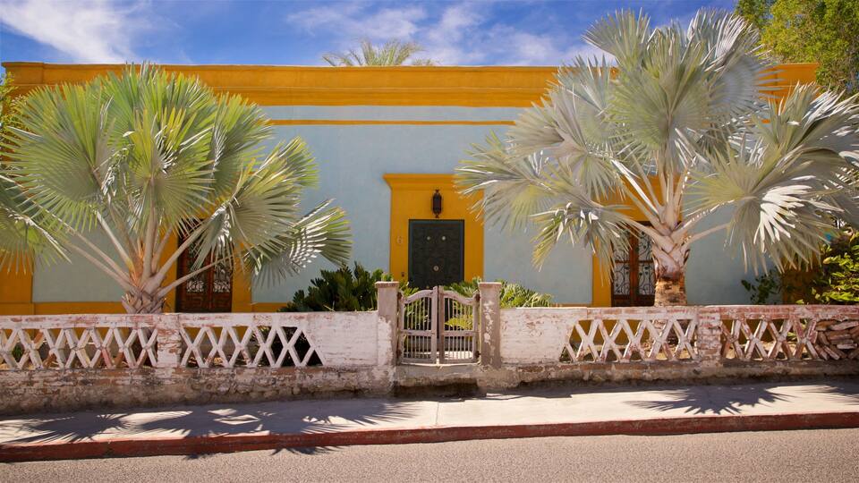 A yellow building with a black door, surrounded by a white fence and palm trees.