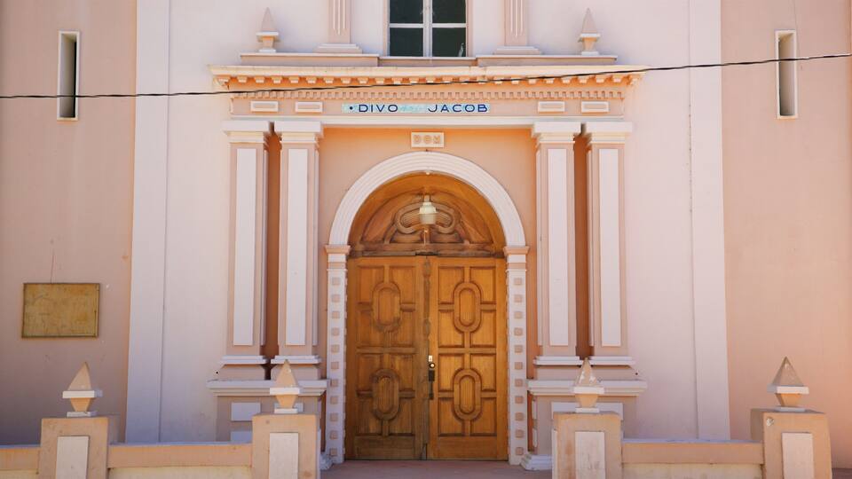 A building facade with a large wooden door, columns, and a sign above the door that reads "DIVO JACOB".